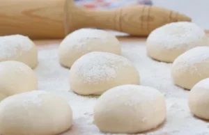 Small rounded portions of dough resting on a baking tray before their final rise.