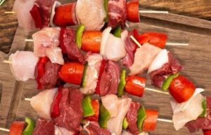 Anticuchos Assembling A close-up of the assembly process, showing marinated meat cubes, onions, and square-cut bell peppers being threaded onto wooden skewers.