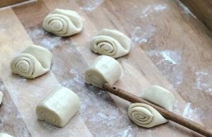 Aseembly of the breads Pressing the center of the rolled dough segments with a wooden spoon handle to create the Bocado de Dama crease.