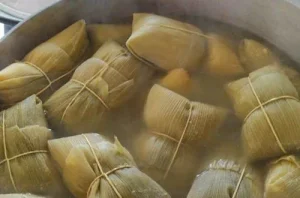 Cooking the humitas Tightly tied corn humitas being submerged in a large pot of simmering water.