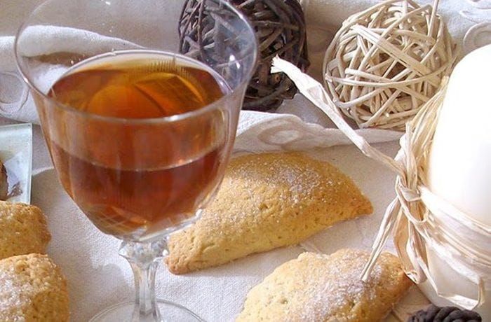 Chilean Canelita — Traditional Cinnamon Mistela Made with Aguardiente and Cinnamon Sticks Glass bottle of Chilean canelita amber cinnamon mistela surrounded by cinnamon sticks and served in small crystal glasses