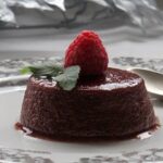 Chilean blackberry flan unmolded onto a plate, showing the glossy dark caramel layer and a garnish of fresh moras on top.