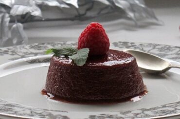 Chilean blackberry flan unmolded onto a plate, showing the glossy dark caramel layer and a garnish of fresh moras on top.