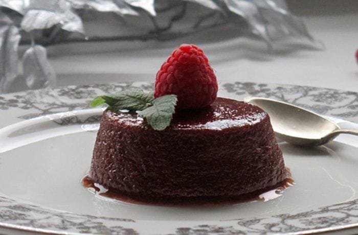Chilean blackberry flan unmolded onto a plate, showing the glossy dark caramel layer and a garnish of fresh moras on top.