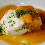 Golden oven-baked corvina fillet covered in a creamy pale-orange sea urchin sauce, garnished with fresh sea urchin tongues and finely chopped chives.