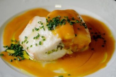 Golden oven-baked corvina fillet covered in a creamy pale-orange sea urchin sauce, garnished with fresh sea urchin tongues and finely chopped chives.