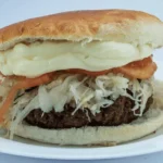 Chilean fricandela (hamburguesa chilena) — seasoned beef patty with avocado, tomato, and mayonnaise on pan frica bread, Santiago soda fountain style