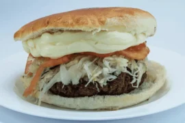 Chilean fricandela (hamburguesa chilena) — seasoned beef patty with avocado, tomato, and mayonnaise on pan frica bread, Santiago soda fountain style