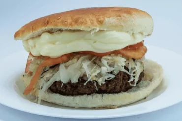 Chilean fricandela (hamburguesa chilena) — seasoned beef patty with avocado, tomato, and mayonnaise on pan frica bread, Santiago soda fountain style