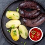 Plate of Chilean prietas served with boiled potatoes and caramelized onions, garnished with fresh parsley.