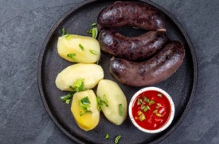 Plate of Chilean prietas served with boiled potatoes and caramelized onions, garnished with fresh parsley.
