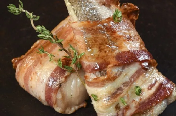Chilean roasted hake fillets wrapped in bacon with bay leaves, butter, and lemon — traditional merluza con tocino recipe
