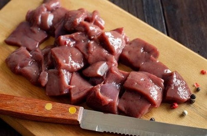 Raw beef liver (pana de vacuno) cut into medium cubes on a cutting board, ready for seasoning and searing
