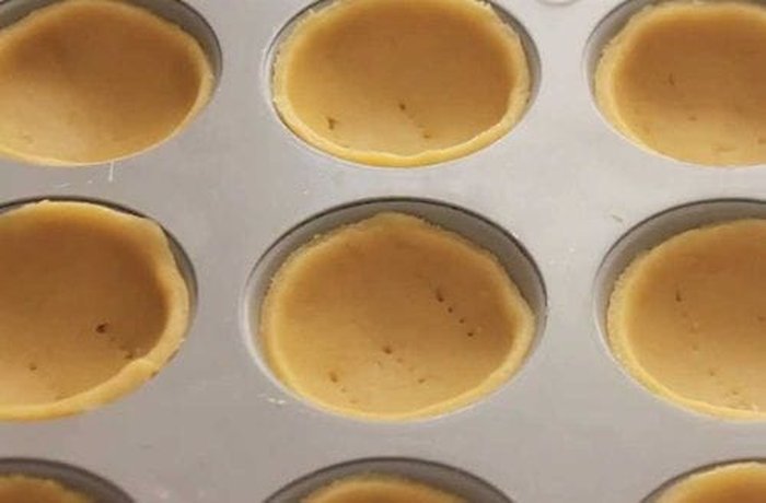 Shaping the pastry dough into small cups inside muffin molds for Chilean tacitas