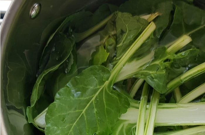 Dark green Swiss chard leaves submerged in a pot of boiling water while blanching