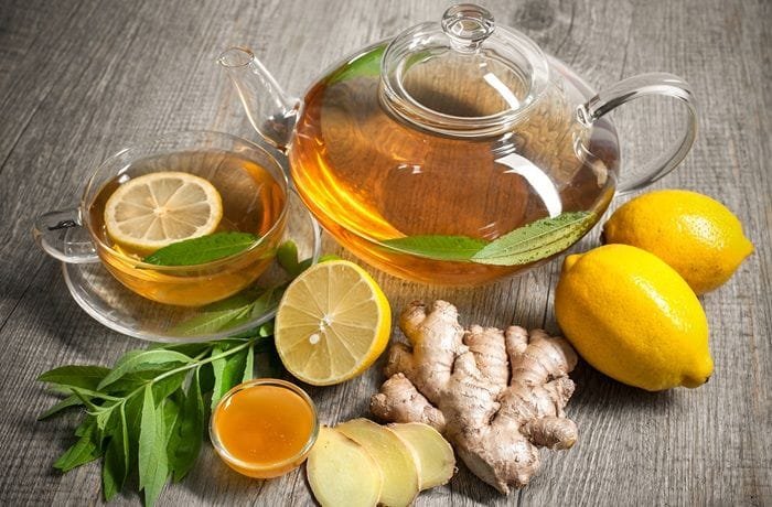 Steaming cup of bariatric tea with floating lemon slices and a cinnamon stick, beside fresh ginger and mint leaves