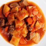 Chilean beef stew with strips of beef, carrot slices, and potatoes in a thick reddish sauce