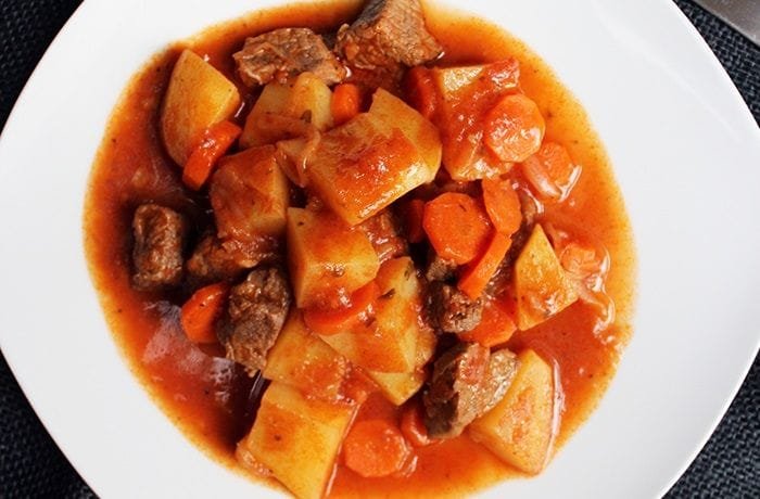 Chilean beef stew with strips of beef, carrot slices, and potatoes in a thick reddish sauce