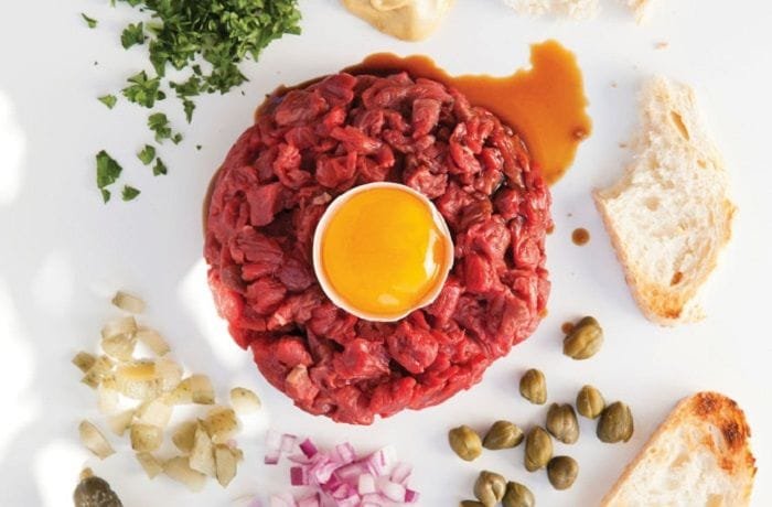 Homemade beef tartare topped with an egg yolk, surrounded by red onion and toast