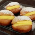 A plate of Chilean fried berlines dusted with powdered sugar and filled with pastry cream.
