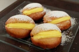 A plate of Chilean fried berlines dusted with powdered sugar and filled with pastry cream.