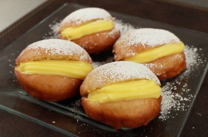 A plate of Chilean fried berlines dusted with powdered sugar and filled with pastry cream.
