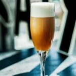 Chilean bitter batido served in a flute glass with dense foam on the surface and a lemon slice.