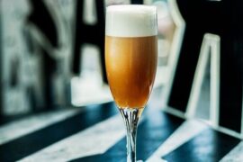 Chilean bitter batido served in a flute glass with dense foam on the surface and a lemon slice.