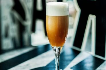 Chilean bitter batido served in a flute glass with dense foam on the surface and a lemon slice.