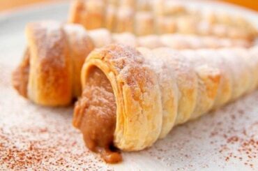 Baked Chilean cachitos filled with manjar, dusted with powdered sugar and grated coconut