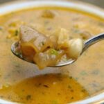A steaming bowl of Chilean pig's feet broth with tender meat and carrots, served with pan amasado bread.
