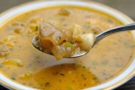 A steaming bowl of Chilean pig's feet broth with tender meat and carrots, served with pan amasado bread.