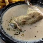 Deep clay bowl of Chilean cazuela nogada with chicken, a whole potato and thick broth with pieces of walnut