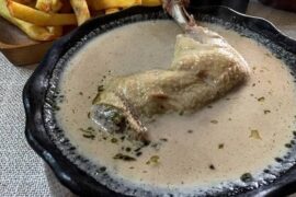 Deep clay bowl of Chilean cazuela nogada with chicken, a whole potato and thick broth with pieces of walnut
