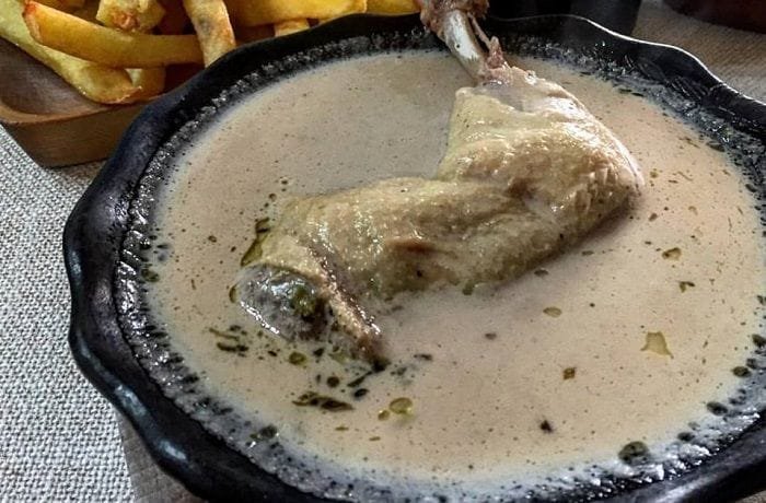 Deep clay bowl of Chilean cazuela nogada with chicken, a whole potato and thick broth with pieces of walnut