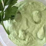 Homemade celery mayonnaise in a bowl, pale green in color, garnished with fresh celery leaves