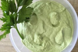 Homemade celery mayonnaise in a bowl, pale green in color, garnished with fresh celery leaves