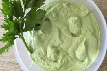 Homemade celery mayonnaise in a bowl, pale green in color, garnished with fresh celery leaves