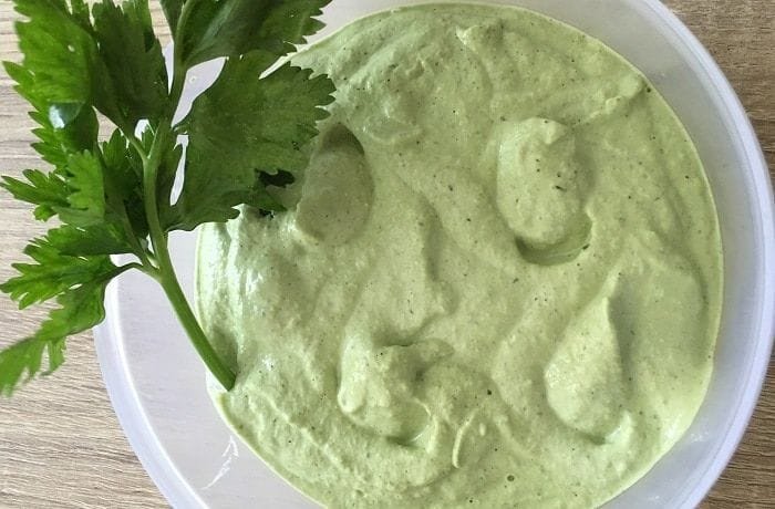Homemade celery mayonnaise in a bowl, pale green in color, garnished with fresh celery leaves