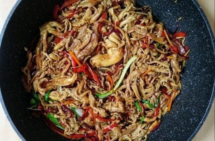 Bowl of noodles with sauteed changles coral mushrooms, bell peppers, and onion