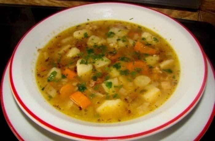Chilean caldo de papas chilotas served in a clay bowl with harina tostada