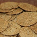 Round whole wheat cochayuyo crackers with dark flecks of seaweed on a wooden surface