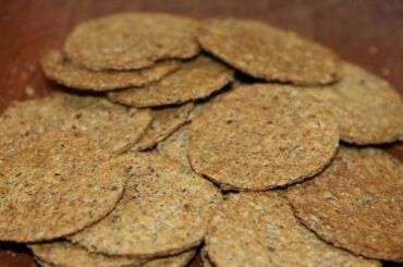 Round whole wheat cochayuyo crackers with dark flecks of seaweed on a wooden surface