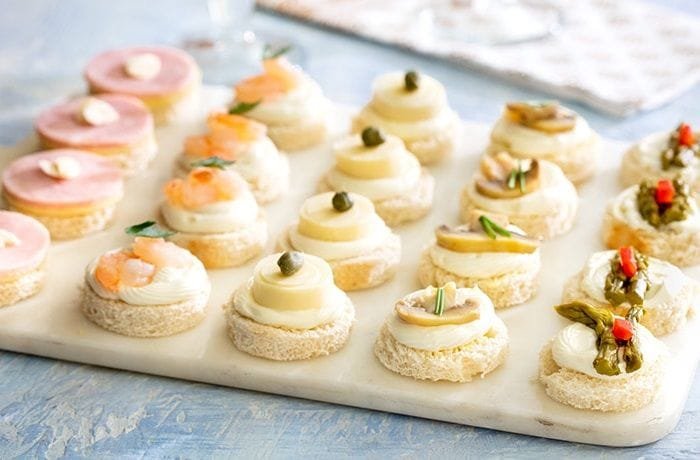 Chilean cold canapés on sandwich bread rounds with salmon, artichoke, and egg toppings