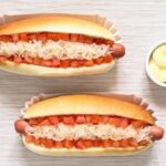 Two Chilean completos with hot dog sausage, tomato, sauerkraut, and mayonnaise on a board