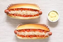 Two Chilean completos with hot dog sausage, tomato, sauerkraut, and mayonnaise on a board