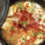 A deep bowl of Chilean concones soup with reddish broth, toasted flour dumplings, and fresh cilantro.