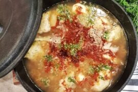 A deep bowl of Chilean concones soup with reddish broth, toasted flour dumplings, and fresh cilantro.