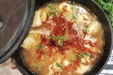 A deep bowl of Chilean concones soup with reddish broth, toasted flour dumplings, and fresh cilantro.