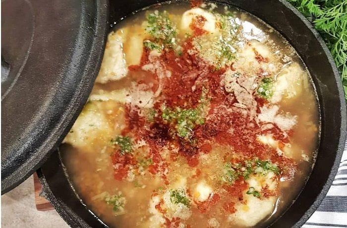 A deep bowl of Chilean concones soup with reddish broth, toasted flour dumplings, and fresh cilantro.